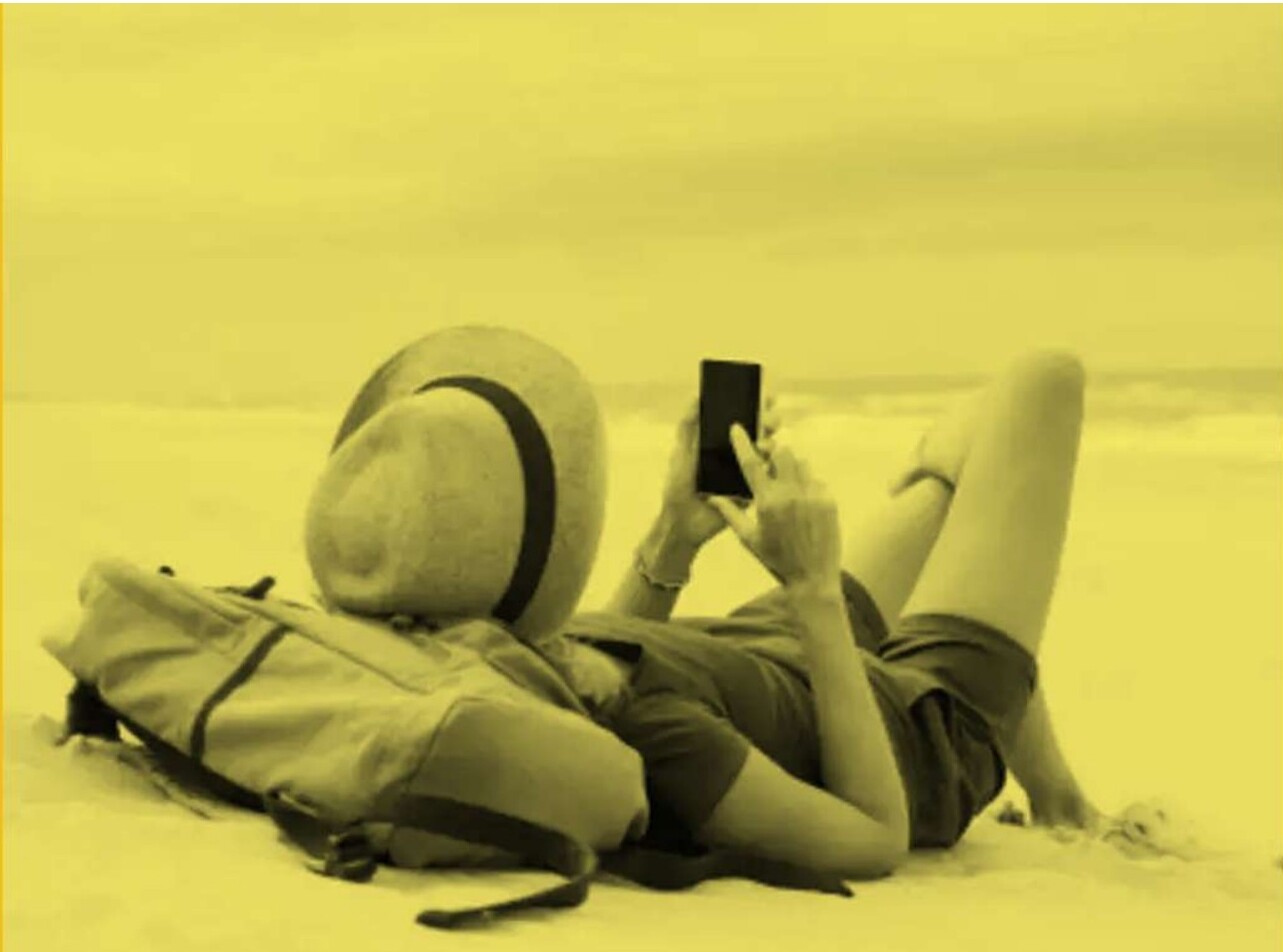 A traveler on a beach planning their next trip on their phone
